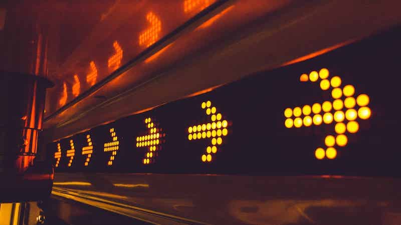 An illuminated signboard featuring multiple right-pointing arrows in a row, each composed of bright orange LED lights. The sign, possibly created through outsourcing, is positioned in a transport or public information setting to direct traffic or indicate a route. CodersLink 2024.