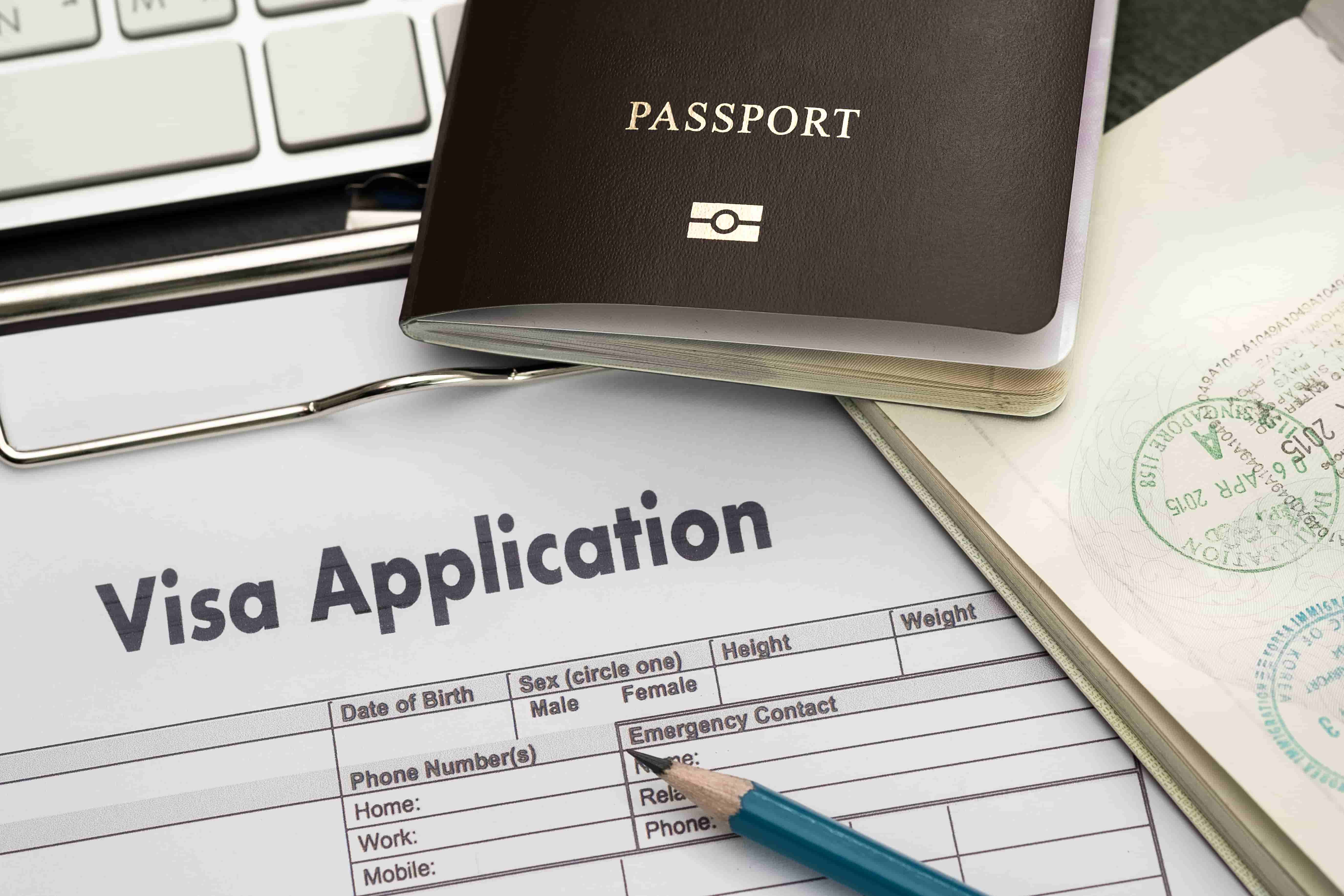 A close-up image of a visa application form placed on a clipboard, alongside a pen and an open passport displaying visa stamps from Latin America. The form includes fields for personal information such as date of birth, sex, phone numbers, and emergency contact details. CodersLink 2024.