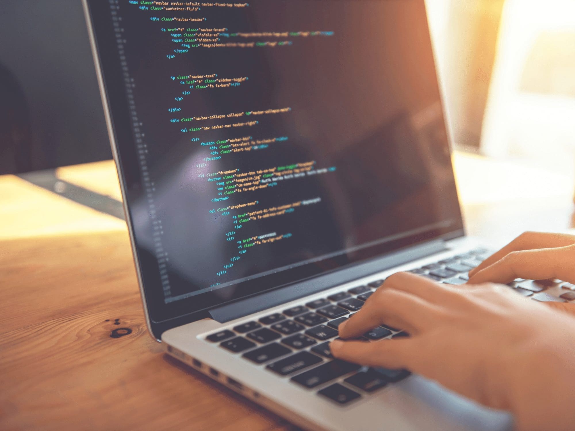 Hands typing on a laptop keyboard, with the screen displaying HTML code. The environment appears to be a well-lit workspace, possibly with natural light coming from a nearby window. The code includes various HTML tags and attributes, suggesting web development activity in the tech industry. CodersLink 2024.