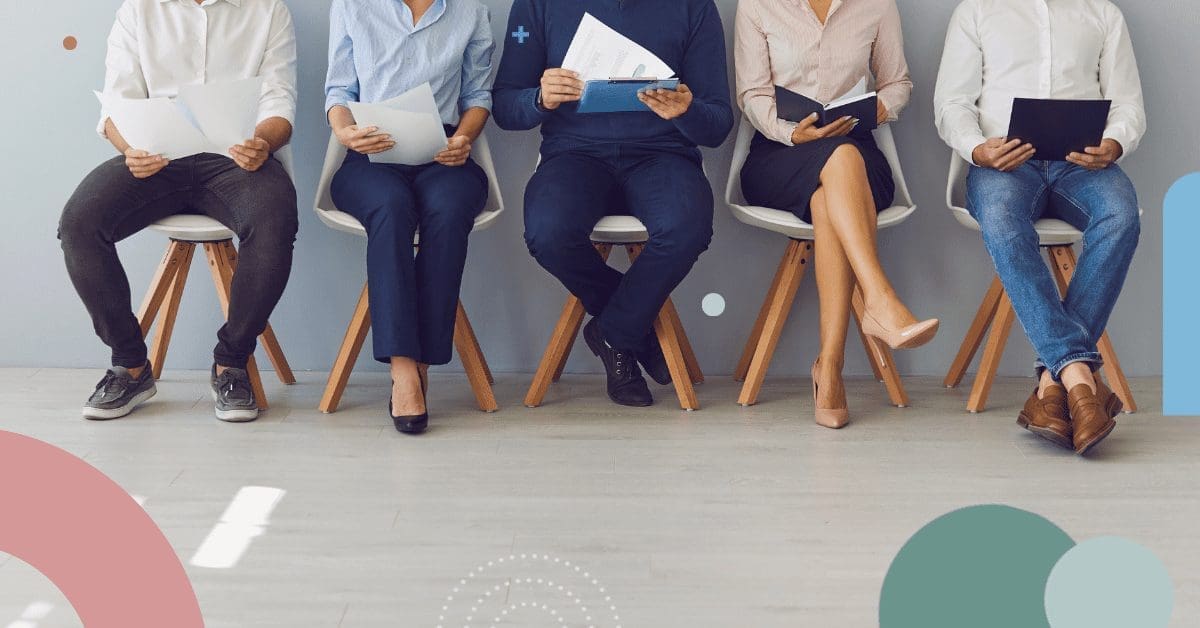 Five individuals sit in a row of chairs, each holding papers or folders, suggesting they might be waiting for an interview. The scene, possibly depicting a hiring process in Colombia, has a neutral background and a light-colored floor that gives it a calm atmosphere. They're dressed in business casual attire. CodersLink 2024.