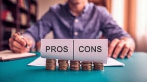 A person sits at a desk with a pen in hand, in front of a sign labeled "PROS" on one side and "CONS" on the other. The sign, balanced on stacks of coins, symbolizes weighing options or considerations typical in Recruitment Process Outsourcing decisions. CodersLink 2024.