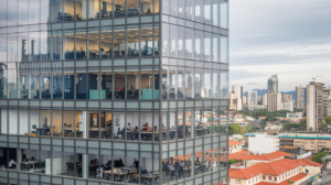 A modern glass office building houses Tech Recruitment Solutions, with multiple floors visible where people diligently work at desks. Situated in an urban area with other buildings and skyscrapers in the background, the scene captures a bustling daytime atmosphere. CodersLink 2024.